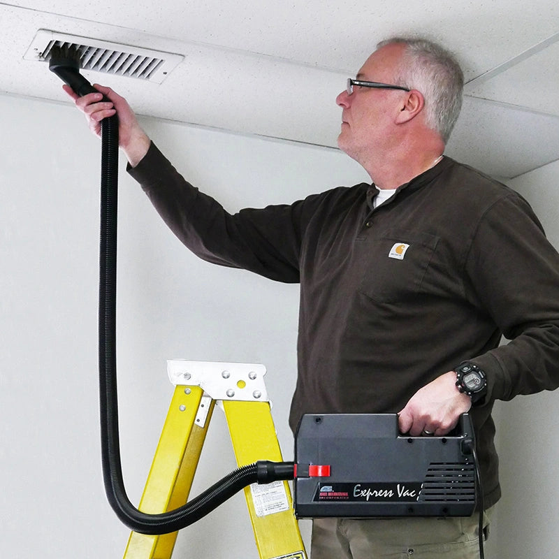 Technician carrying an Atrix VACEXP-04 and using its hose to clean an overhead grille