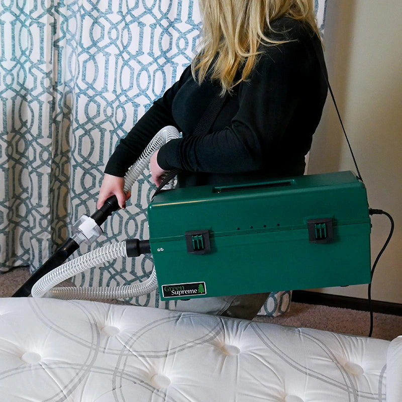 Operator using the Atrix VACOMEGASIPM green vacuum and clear hose beside a mattress