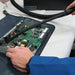 Technician using the Atrix VACOMEGASLFH hose and crevice tool around an exposed circuit board