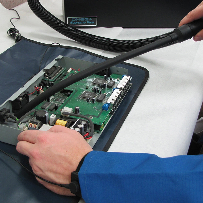 Technician using the Atrix VACOMEGASLFH hose and crevice tool around an exposed circuit board